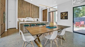 Uma cozinha moderna com armários de madeira, uma ilha central e uma área de refeições com uma mesa grande e cadeiras brancas.