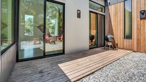 Uma casa moderna com grandes portas de vidro deslizantes, um deck de madeira e uma churrasqueira.