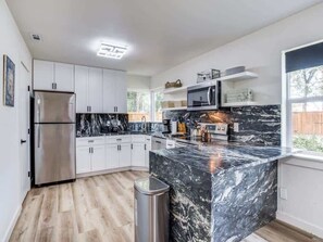 A modern kitchen with white cabinets, a black marble island, stainless steel appliances, and a window providing natural light.