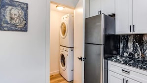 Uma cozinha compacta com geladeira de aço inoxidável, máquina de lavar e painel de fundo de mármore.
