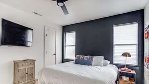 Quarto com cama, ventilador de teto, televisão, guarda-roupa e mesa de cabeceira com abajur.