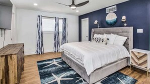 Une chambre à coucher comprenant un lit, un ventilateur de plafond, une table de chevet et une commode en bois.