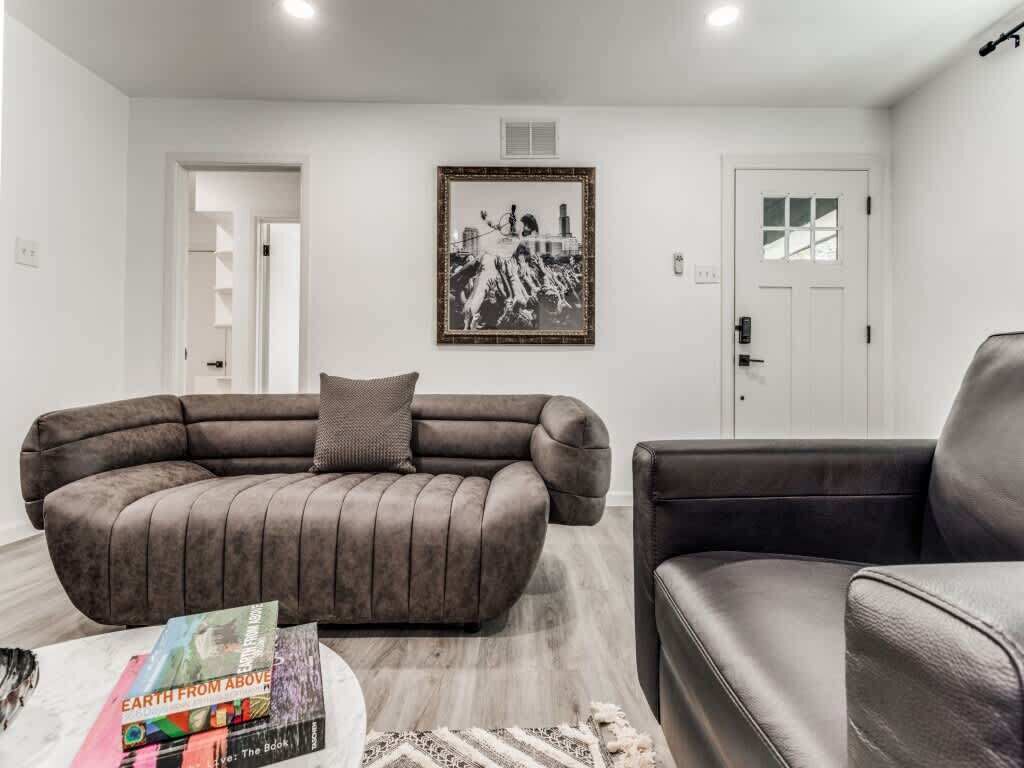A living room with a large L-shaped sofa, a smaller armchair, a coffee table with a book, and a framed picture on the wall.
