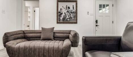 A living room with a large L-shaped sofa, a smaller armchair, a coffee table with a book, and a framed picture on the wall.