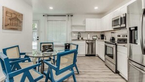 Una cocina moderna con armarios blancos, electrodomésticos de acero inoxidable y una mesa de comedor de vidrio con sillas azules.