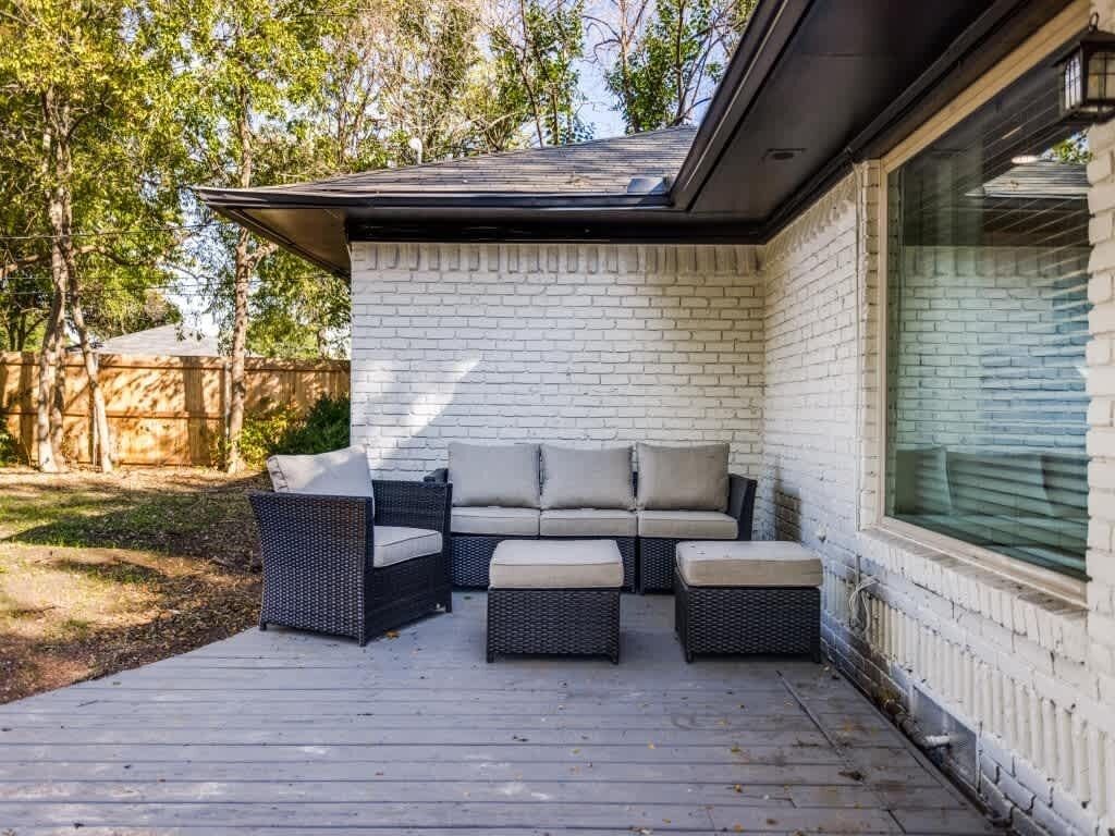 Een overdekt terras met een witte bakstenen muur, een zwarte wicker loungeset en een raam met zonwering.