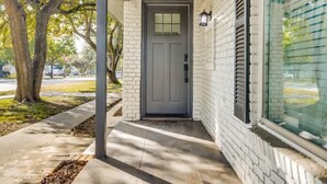 Una casa con puerta gris, fachada de ladrillo blanco y un porche cubierto.