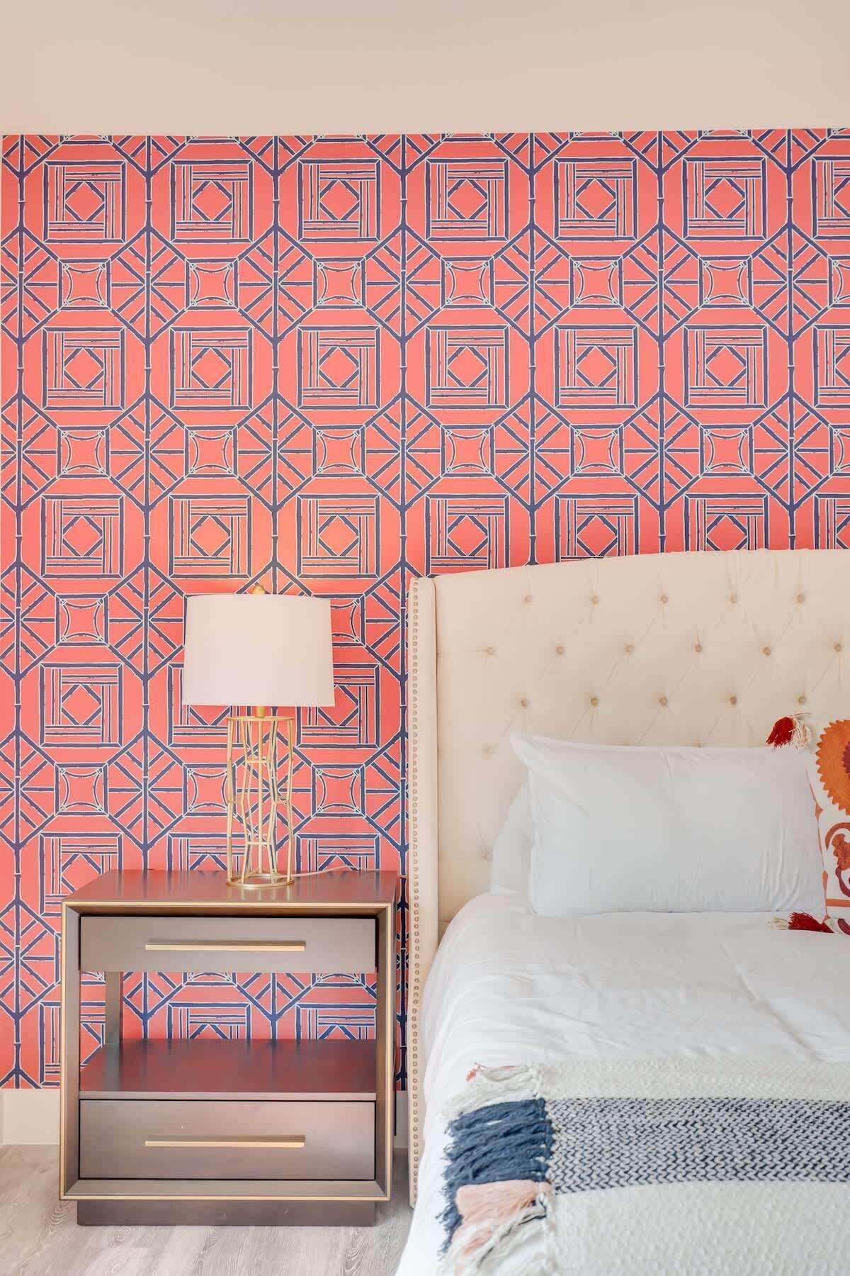 Une chambre à coucher avec un papier peint à motifs, une table de chevet avec une lampe, un lit avec une literie blanche et une commode.