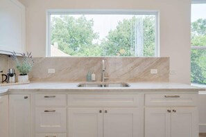 A kitchen with a large window, a sink, and cabinets.