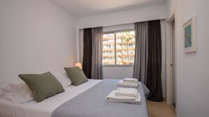 A hotel room with a bed, pillows, a quilted bedspread, a window with curtains, a framed picture on the wall, and a view of a building outside. - Ref: 278  Beach apartment with pool and parking (Fuengirola)