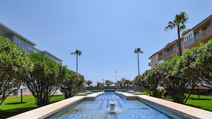 A swimming pool with a water fountain, surrounded by well-maintained greenery and modern buildings. - Ref: 278  Beach apartment with pool and parking (Fuengirola)