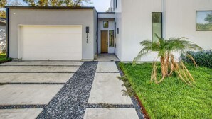 Un bâtiment moderne doté d’un garage, d’un chemin menant à l’entrée et d’une pelouse bien entretenue avec un palmier.