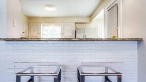 A kitchen with white cabinets, a wooden countertop, and two glass bar stools.