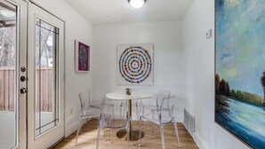 A room with a round table, clear chairs, a painting on the wall, and a door with glass panels.