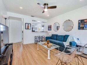 A modern living room with a sofa, coffee table, and chairs, a television, and artwork on the walls. - Preston Hollow Bungalow | Huge Yard (Dallas)