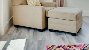 Ein modernes Wohnzimmer mit einer Couch und Hocker, einem Fenster mit Vorhängen und einem farbenfrohen abstrakten Gemälde an der Wand.