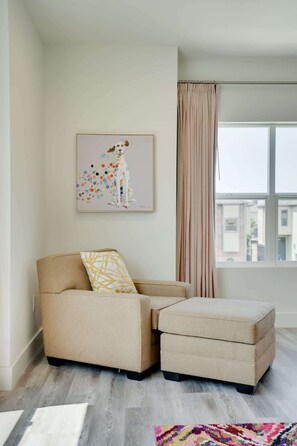 A modern living room with a sofa and ottoman, a window with curtains, and a colorful abstract painting on the wall. - Driem House |Chic | Highland Park Adjacent (Dallas)