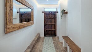 Un pasillo con una puerta de madera, un espejo grande, un banco y un tapete estampado.