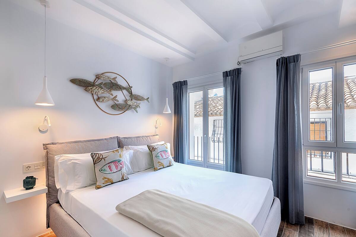 Un dormitorio con una cama grande, dos mesitas de noche, un adorno de pez en la pared, una ventana con cortinas y un equipo de aire acondicionado.