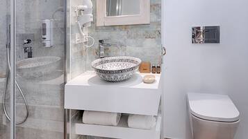 Un baño moderno con ducha envuelta en vidrio, un lavamanos grande de pedestal, un espejo y un inodoro.
