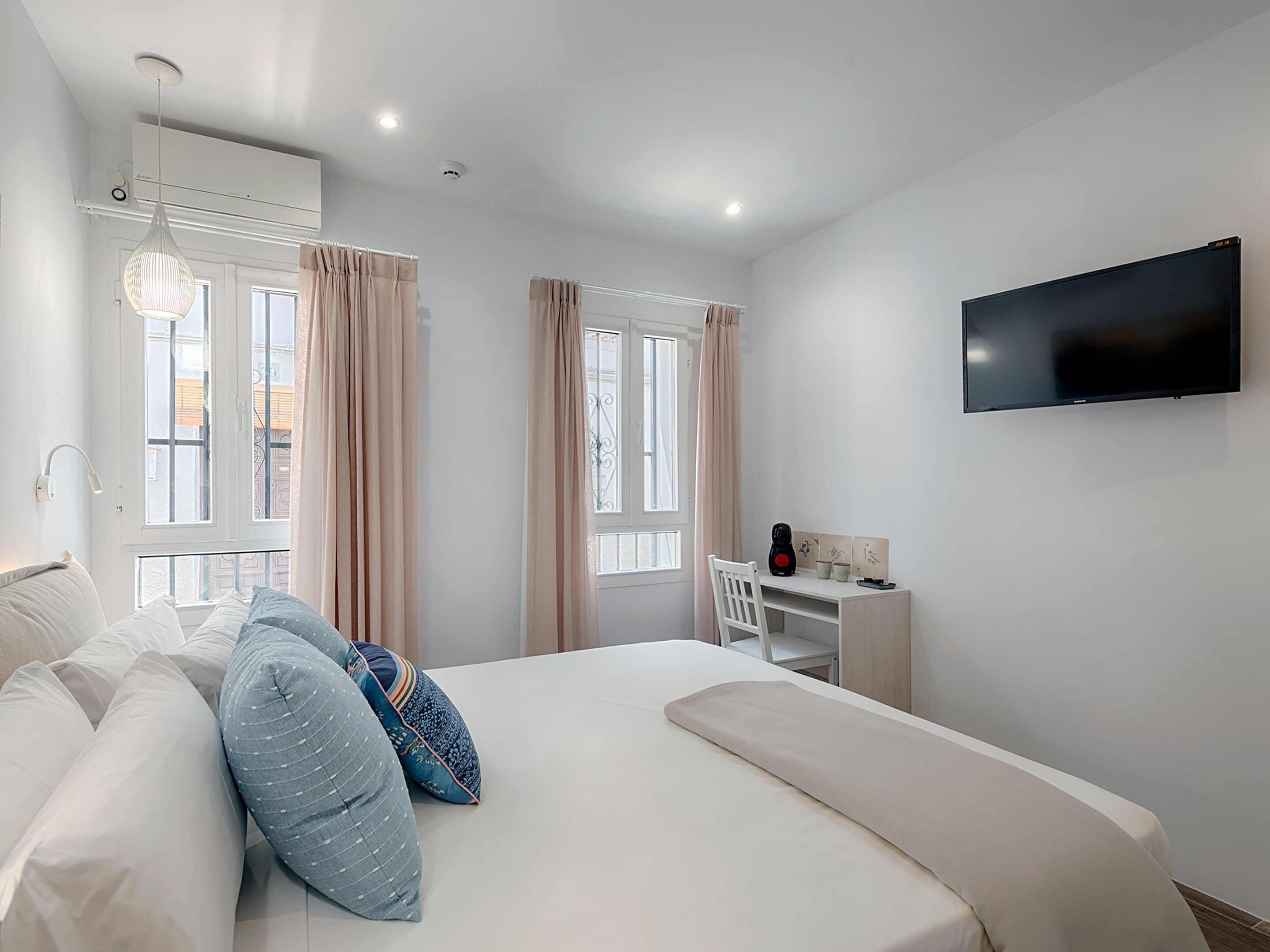 A modern bedroom with a bed, a desk, a television, and windows with curtains.