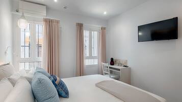 A modern bedroom with a bed, a desk, a television, and windows with curtains.