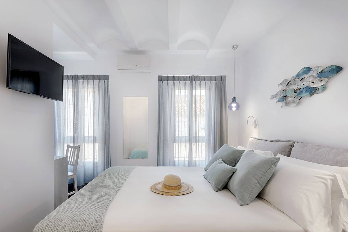 Un dormitorio con cama, televisor montado en la pared, ventana con cortinas y lámpara de pared.