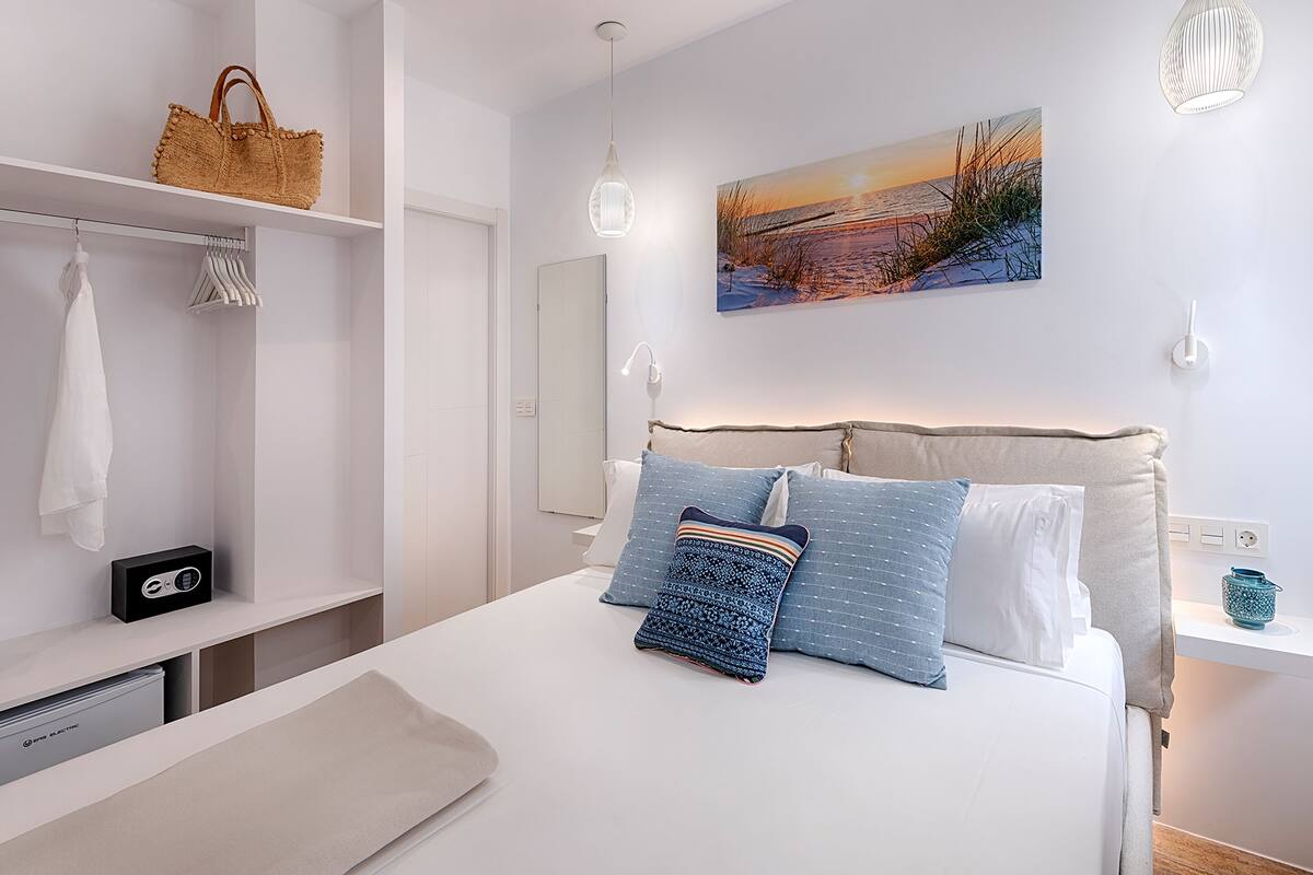 Un dormitorio moderno con cama, mesita de noche, armario y una lámpara colgante, además de un cuadro en la pared.