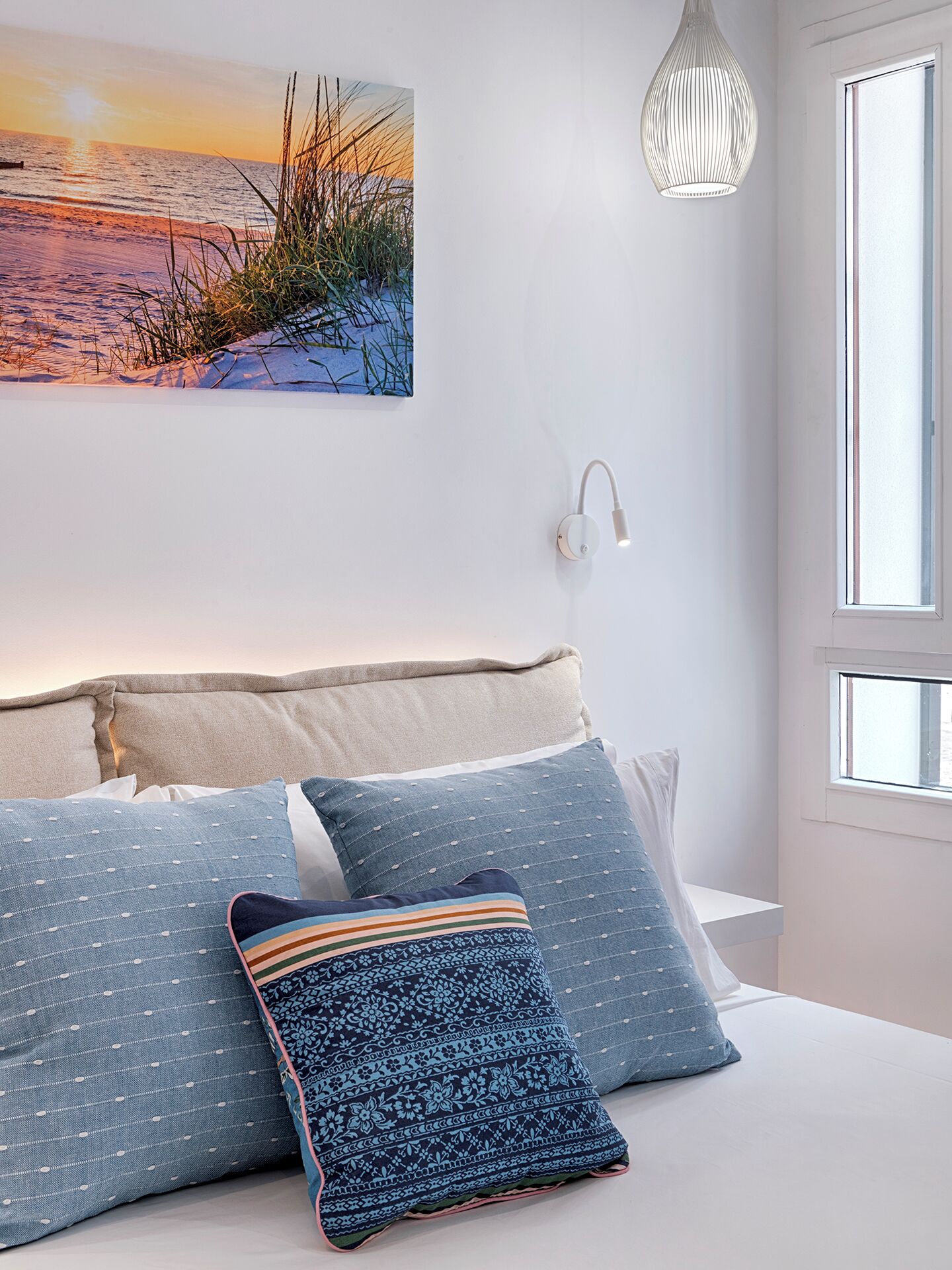 Un dormitorio con cama, almohadas, una lámpara de pared y una ventana.
