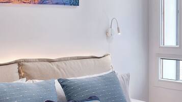 Un dormitorio con cama, almohadas, una lámpara de pared y una ventana.