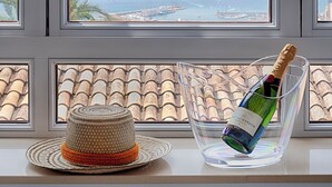 Una ventana con vistas a un paisaje costero, una botella de champán y un sombrero de paja en el alféizar.