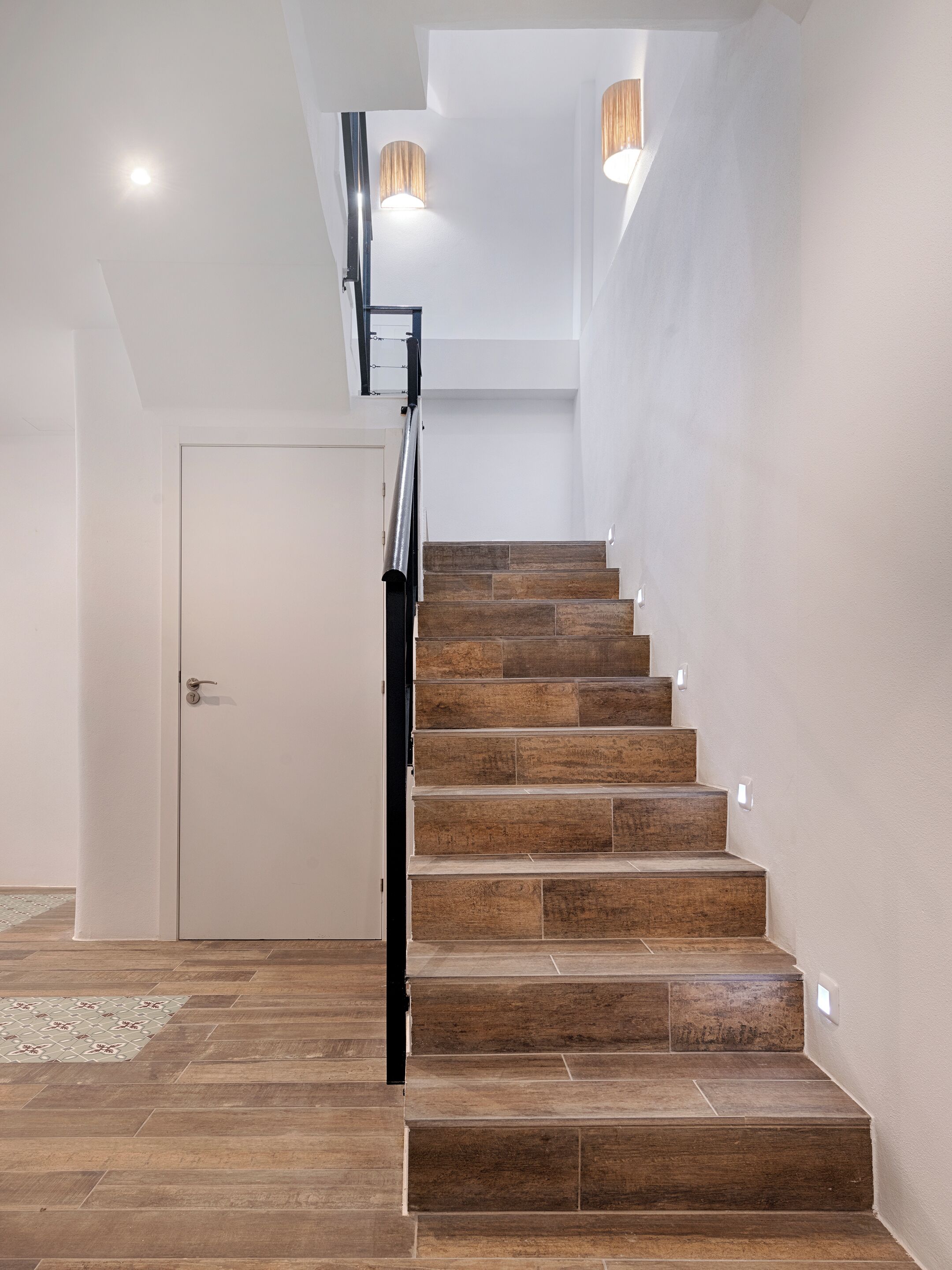 A staircase with wooden steps and a metal railing, leading to a landing with a white door.