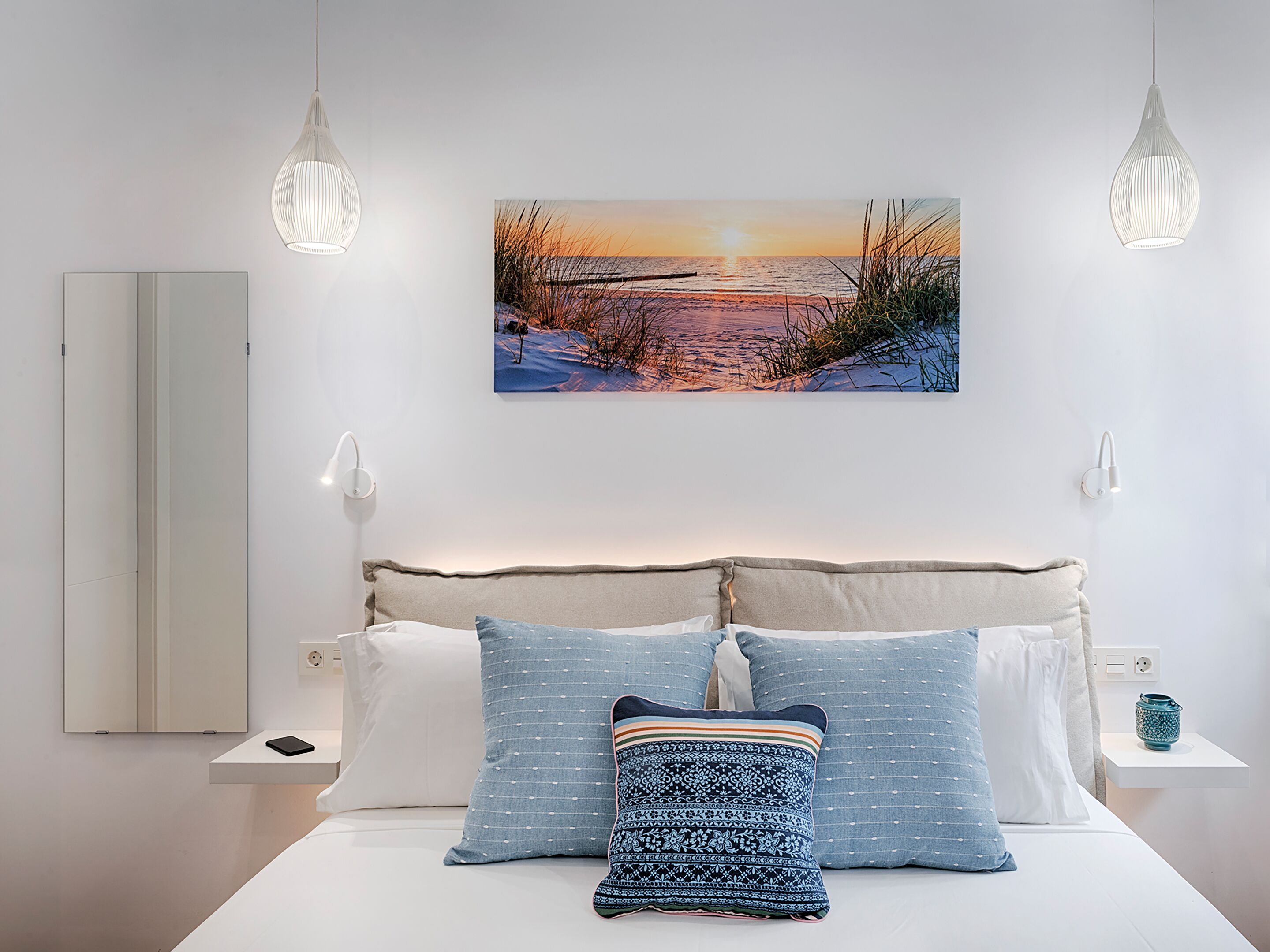 A modern bedroom with a large bed, two bedside tables, a wall-mounted picture, and pendant lights.