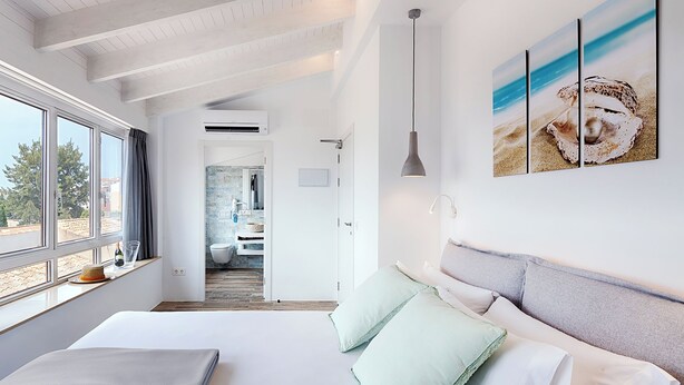 Un dormitorio moderno con una cama grande, vistas a la ciudad y una obra de arte con temática playera en la pared.