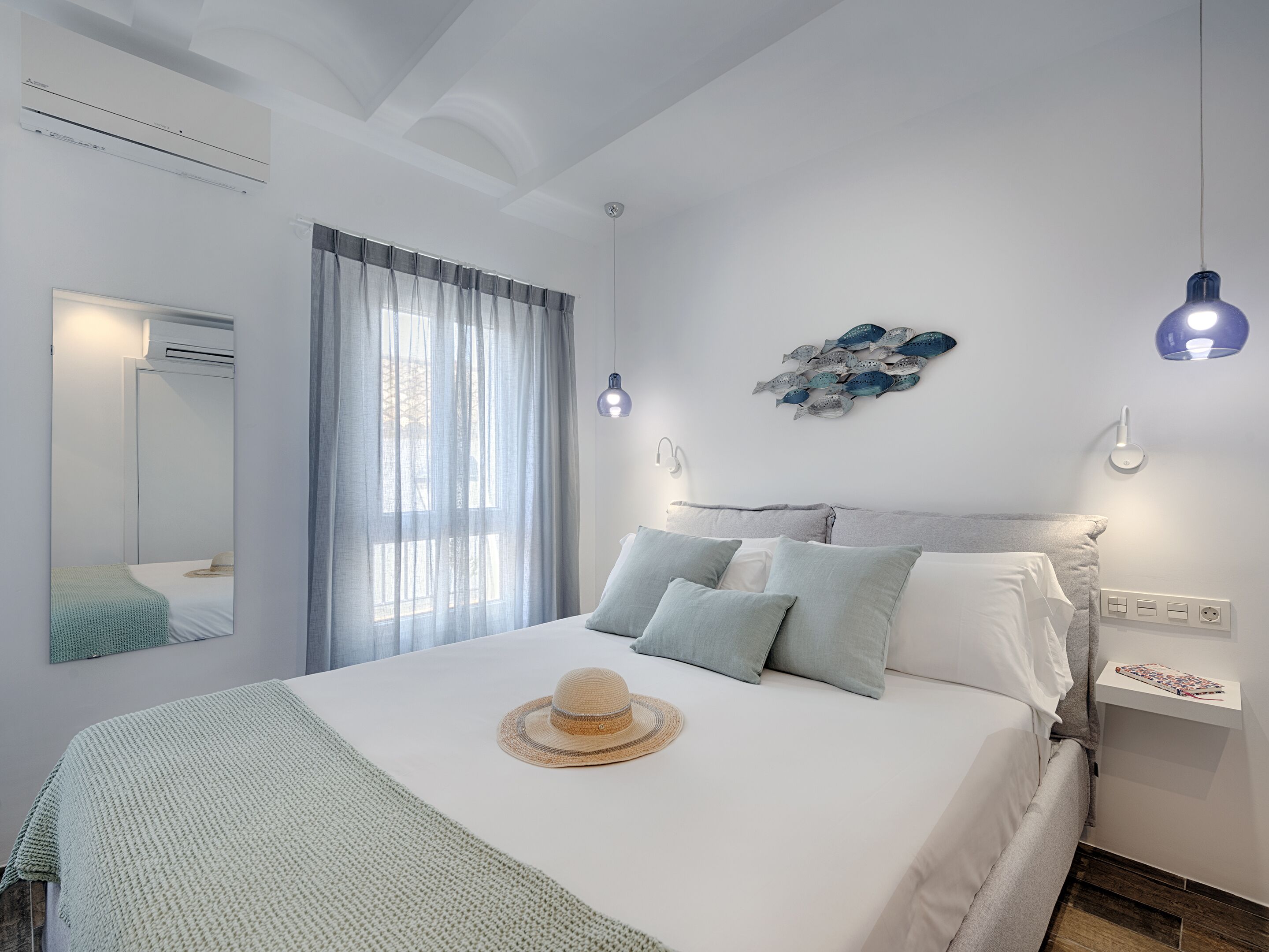 A bedroom with a bed, a window with sheer curtains, a wall-mounted light fixture, and a wall art piece.