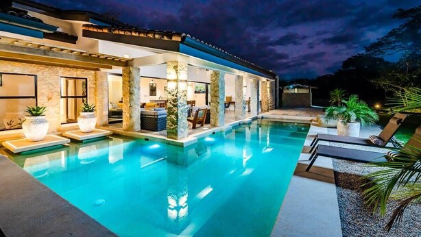 A modern poolside area with a clear pool, stone pillars, and lounge chairs.