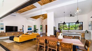 A spacious living area with a wooden dining table, yellow sofa, and a large TV.