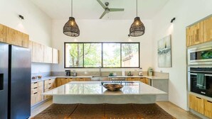 A modern kitchen with a central island, wooden cabinets, stainless steel appliances, and pendant lighting.