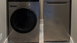 Une cuisine compacte dotée d’un lave-linge et d’un sèche-linge intégrés, d’un réfrigérateur en acier inoxydable et d’un dosseret carrelé.