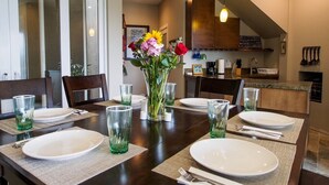 Une table à manger dressée pour six personnes, avec de la vaisselle en verre transparent, des assiettes et un vase rempli de fleurs.