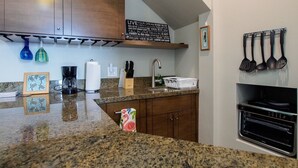 Une cuisine dotée de plans de travail en granit, de meubles en bois, d’une machine à café, d’un grille-pain et d’un porte-ustensiles suspendu.