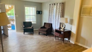 A room with a wooden floor, a brown armchair, a desk with a lamp, and a window with curtains. - Ocean One Inn (Sneads Ferry)