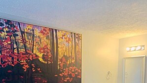 A bedroom with a bed, a desk, a chair, a painting, a bathroom with a sink and mirror. - Ocean One Inn (Sneads Ferry)