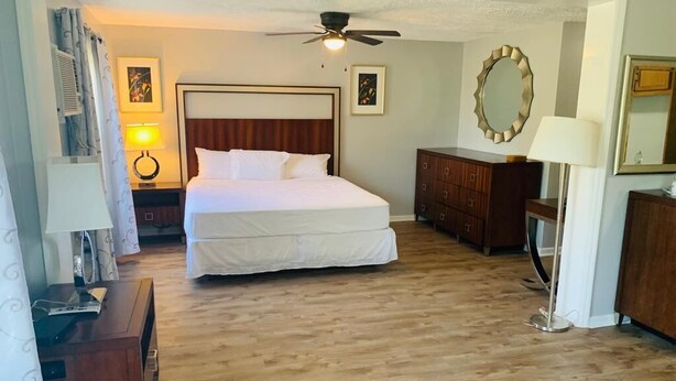 A hotel room with a large bed, a ceiling fan, wooden flooring, a dresser, and a mirror. - Ocean One Inn (Sneads Ferry)