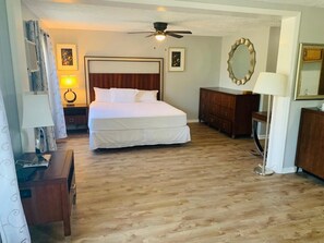 A hotel room with a large bed, a ceiling fan, wooden flooring, a dresser, and a mirror. - Ocean One Inn (Sneads Ferry)