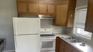 A kitchen with wooden cabinets, a white refrigerator, a stove, and a sink. - Ocean One Inn (Sneads Ferry)