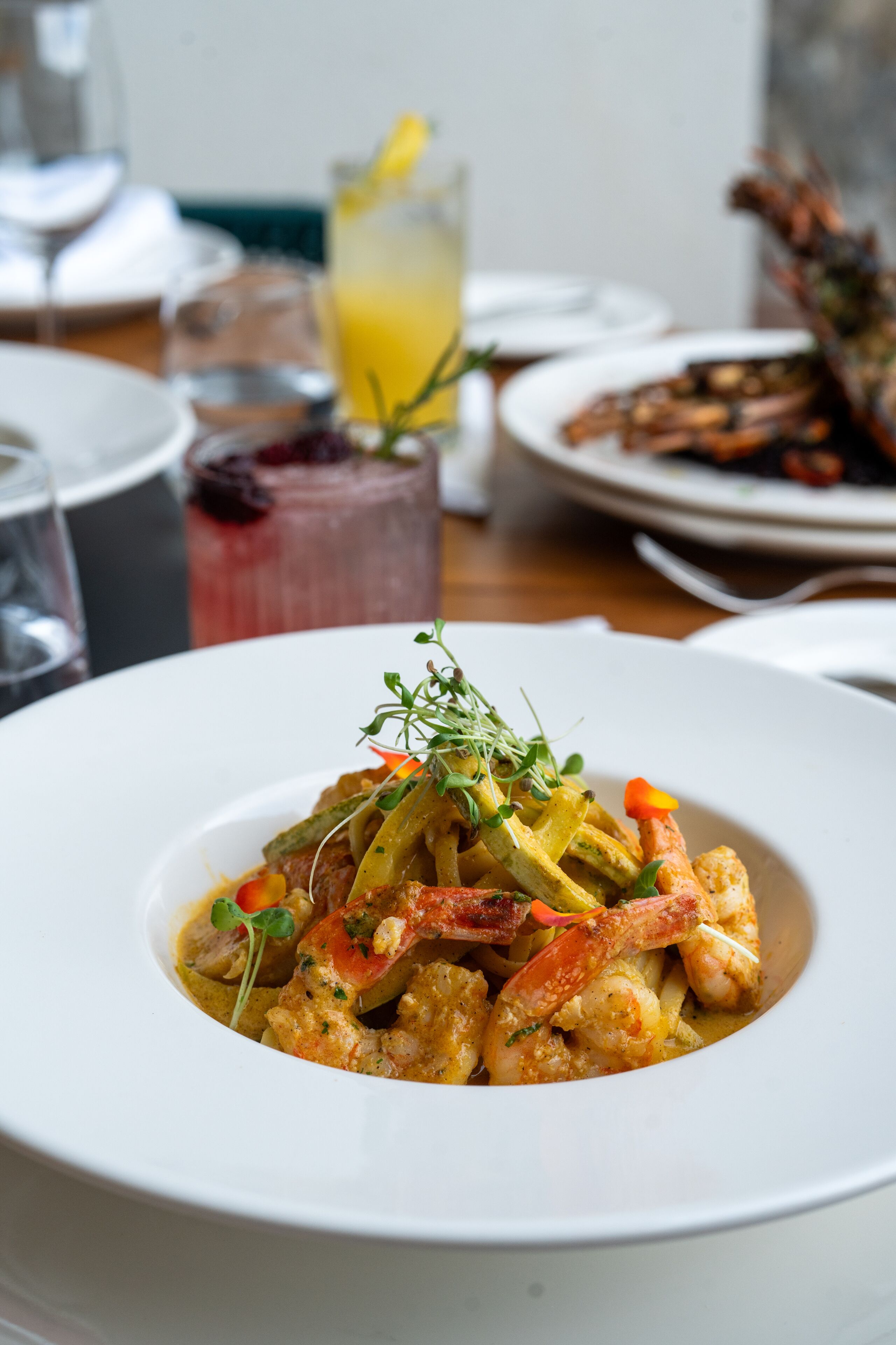 A white plate with a seafood dish garnished with herbs, accompanied by a glass of orange juice and a glass of red wine on the table.