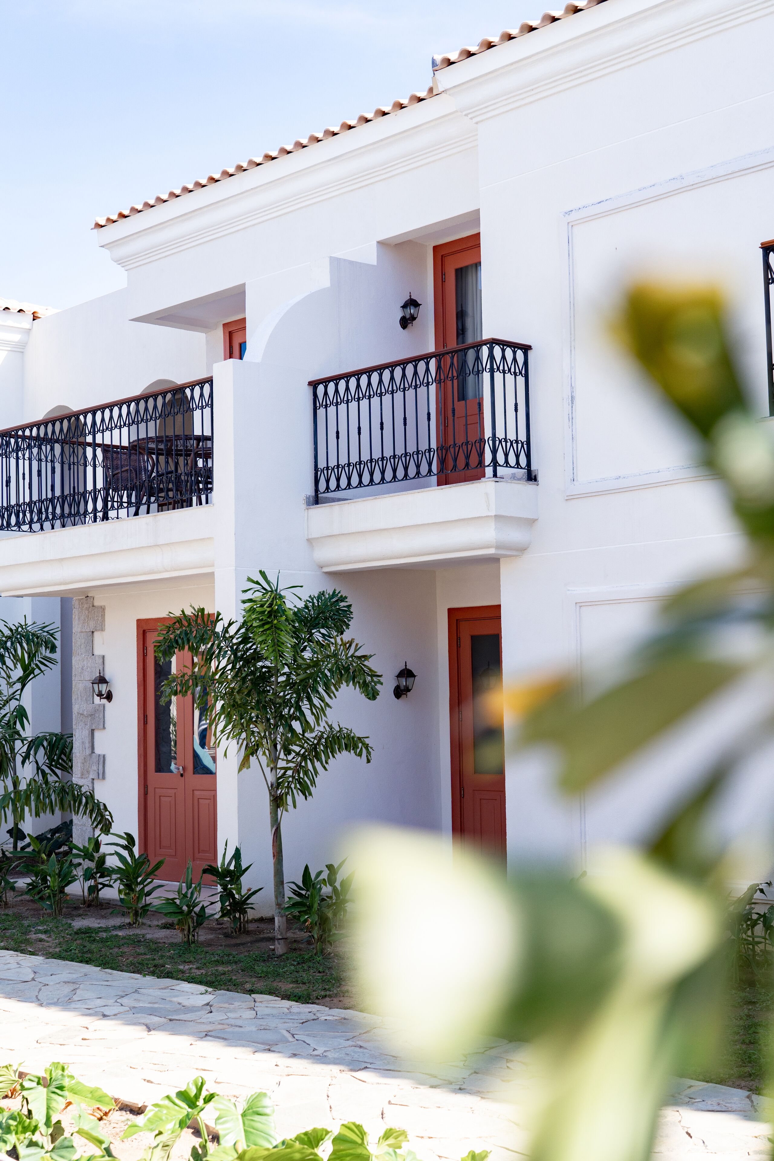 A two-story building with balconies, a stone-paved entrance, and small trees.
