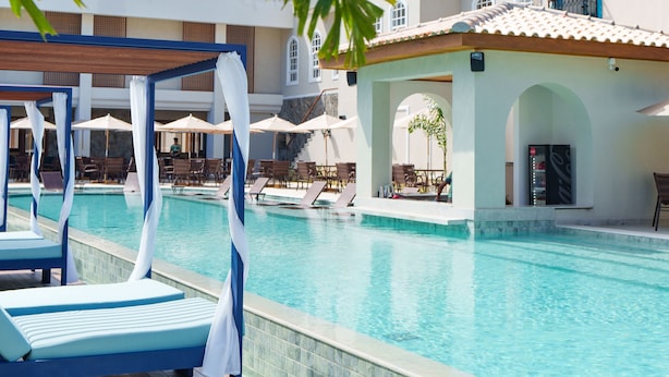 A swimming pool with lounge chairs and umbrellas, surrounded by a building with a tiled roof and white walls. - Resende Imperial Hotel &Spa (Itacaré)