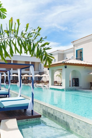 A swimming pool with lounge chairs and umbrellas, surrounded by a building with a tiled roof and white walls. - Resende Imperial Hotel &Spa (Itacaré)